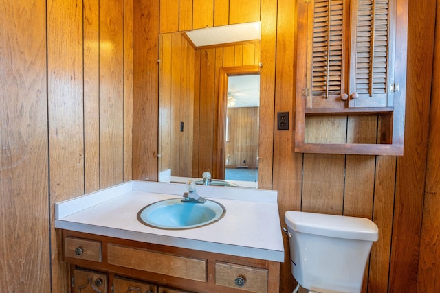 half bathroom featuring wooden walls, vanity, and toilet