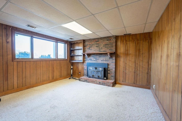 unfurnished living room with a paneled ceiling, visible vents, wood walls, and carpet floors