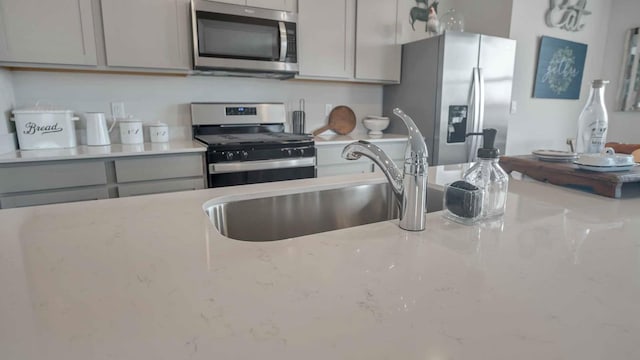 kitchen with a sink, light stone countertops, gray cabinets, and stainless steel appliances