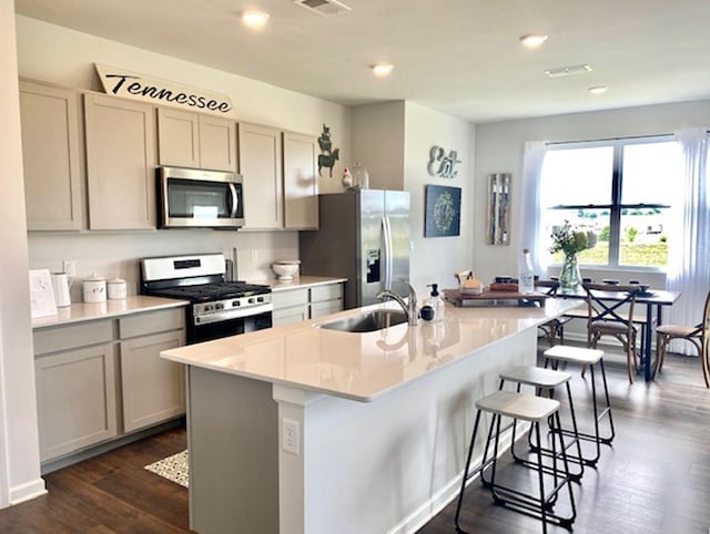 kitchen with a breakfast bar area, a kitchen island with sink, a sink, dark wood-type flooring, and appliances with stainless steel finishes