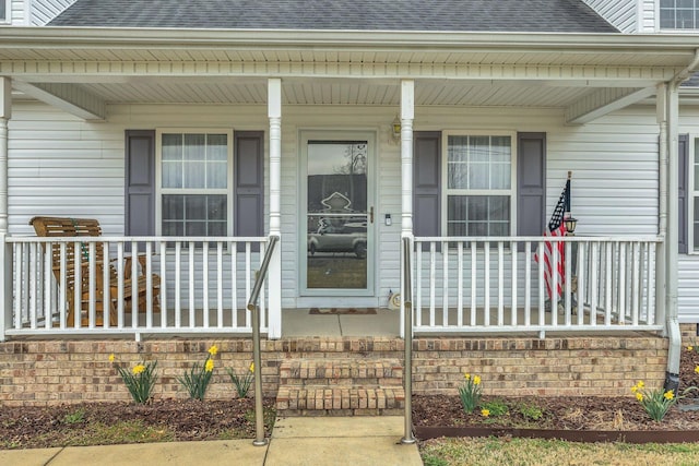 doorway to property with covered porch and a shingled roof