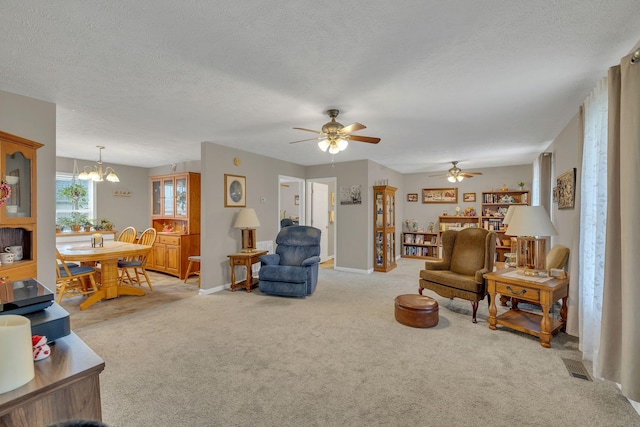 living room featuring visible vents, ceiling fan with notable chandelier, a textured ceiling, baseboards, and light colored carpet