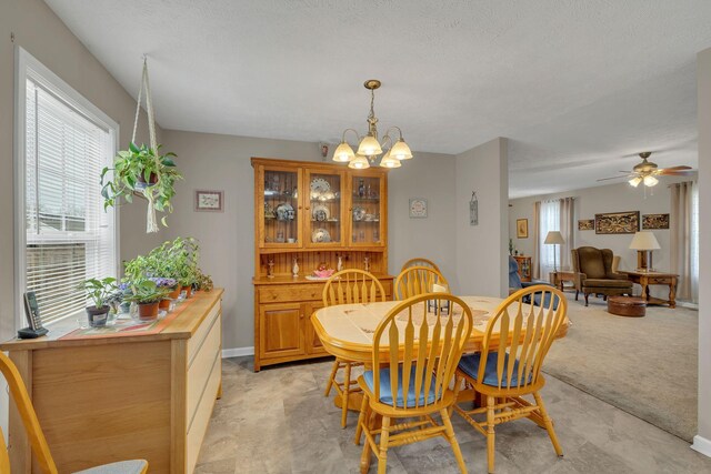 dining room with ceiling fan with notable chandelier, a healthy amount of sunlight, light colored carpet, and baseboards