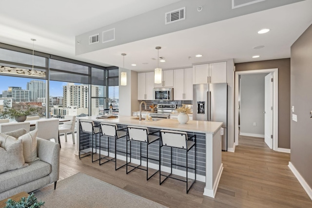 kitchen with visible vents, a kitchen bar, wood finished floors, white cabinetry, and appliances with stainless steel finishes