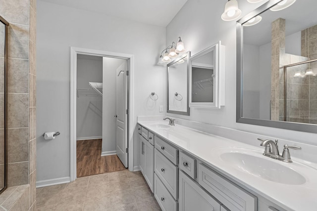 bathroom featuring a spacious closet, a tile shower, double vanity, and a sink