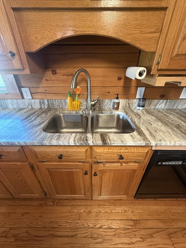 kitchen with dishwasher, light stone counters, brown cabinets, and a sink