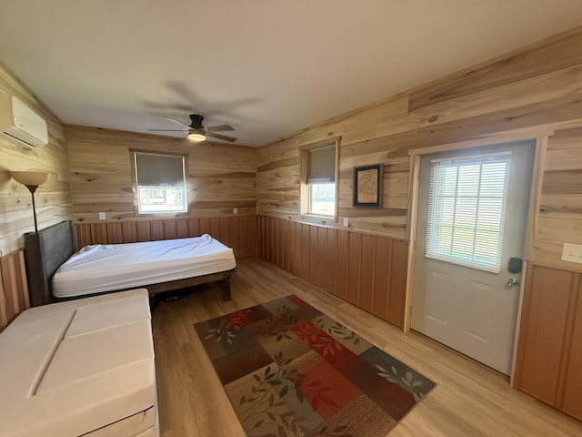 bedroom with light wood finished floors, wooden walls, ceiling fan, and a wall mounted AC