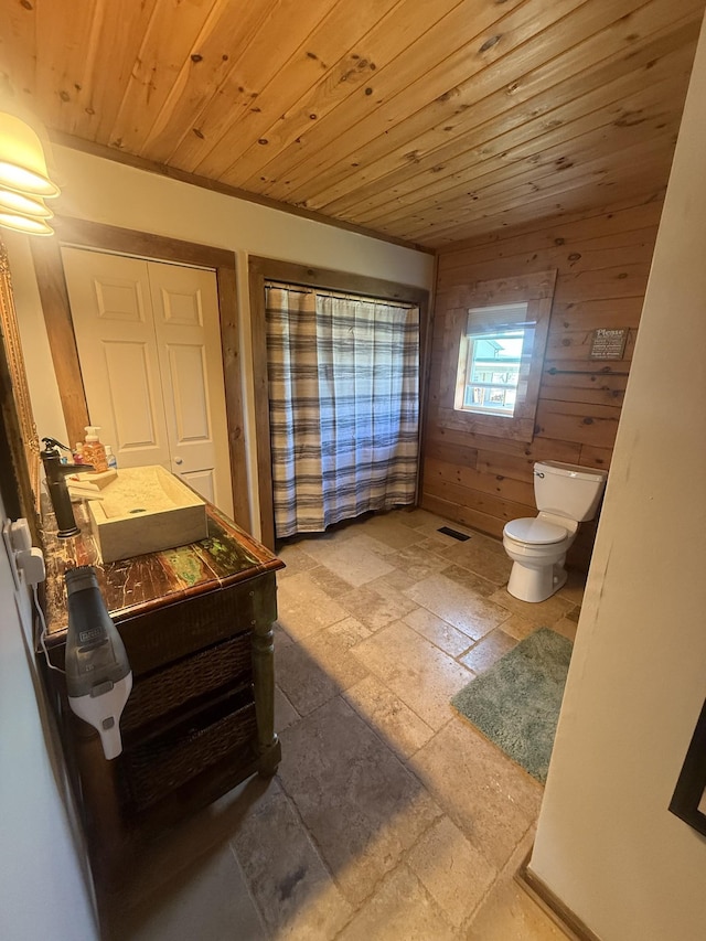 bathroom with visible vents, toilet, stone tile floors, wooden ceiling, and wood walls
