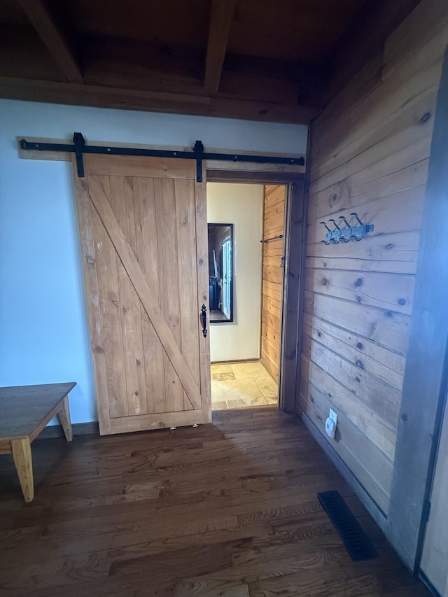 hall featuring visible vents, wood walls, a barn door, and wood finished floors