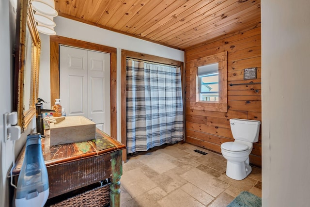 full bathroom with stone tile floors, wooden walls, visible vents, wooden ceiling, and toilet