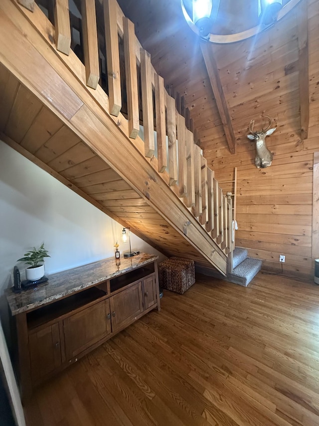 stairway with lofted ceiling with beams, wood finished floors, wooden ceiling, and wood walls