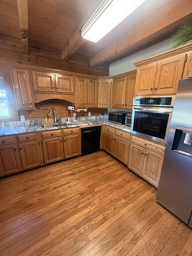 kitchen with brown cabinetry, a sink, stainless steel appliances, light wood-style floors, and beamed ceiling