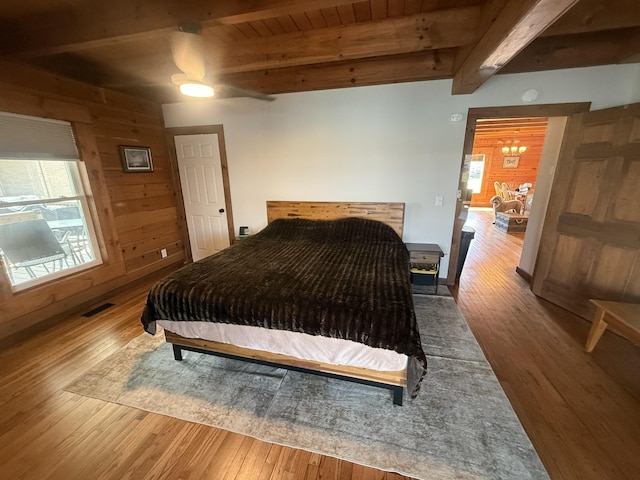 bedroom featuring wooden walls, wood finished floors, visible vents, wood ceiling, and beamed ceiling