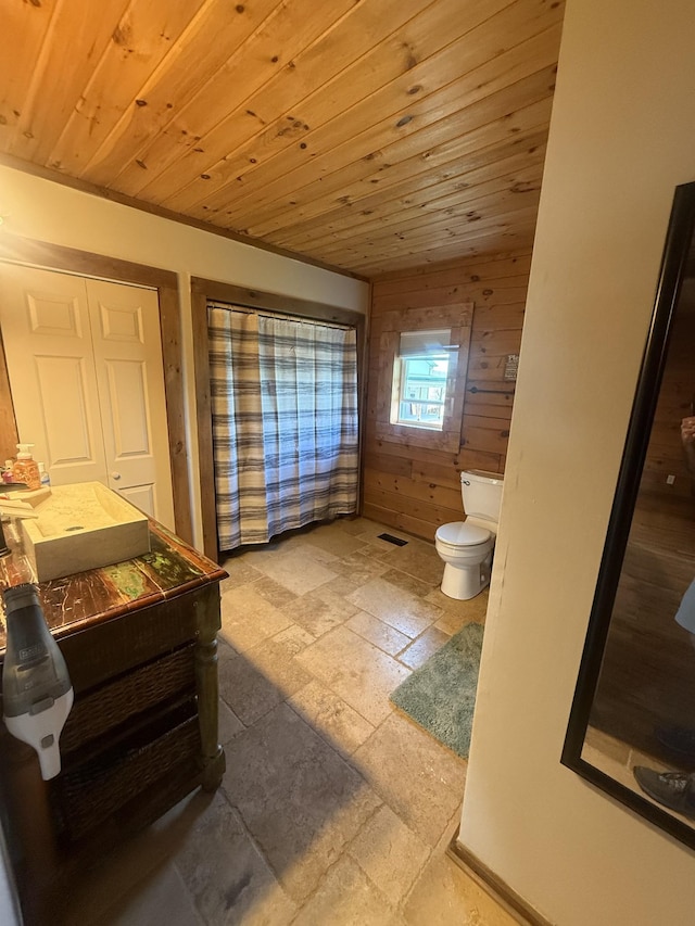 bathroom with toilet, wood ceiling, wooden walls, and stone tile floors