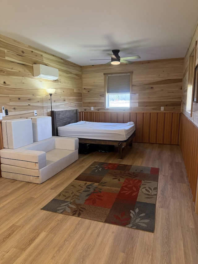 bedroom featuring a wall unit AC, wooden walls, wood finished floors, and ceiling fan