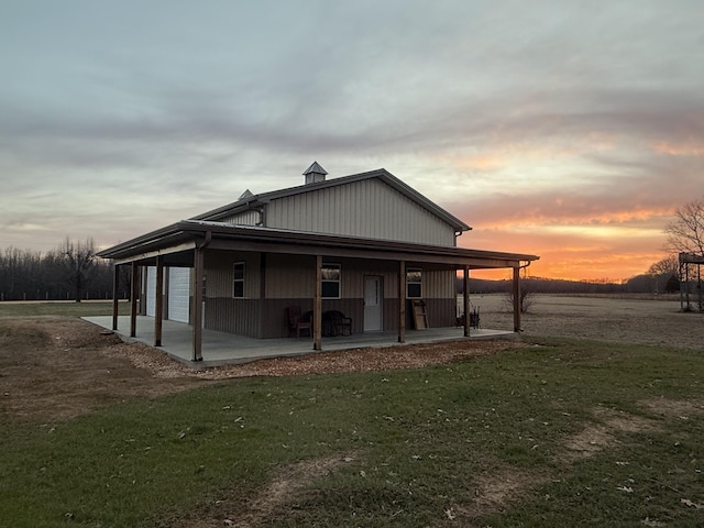 back of house at dusk featuring a lawn, a porch, and a garage