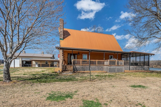 view of front of house featuring a water view, a front yard, covered porch, metal roof, and a sunroom