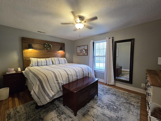 bedroom featuring wood finished floors, visible vents, baseboards, ceiling fan, and a textured ceiling