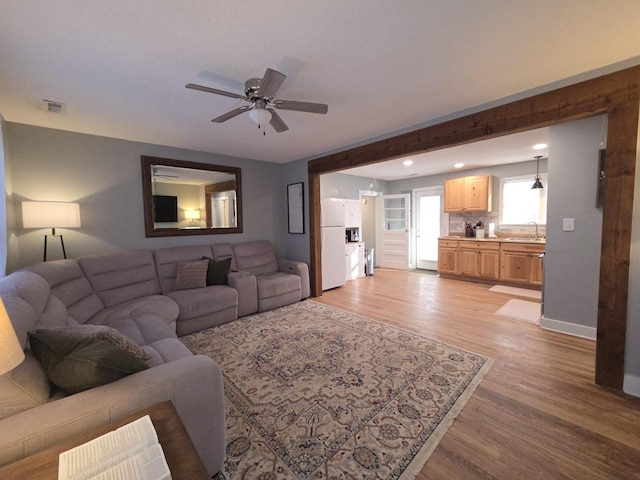 living room featuring visible vents, light wood-style flooring, baseboards, and a ceiling fan