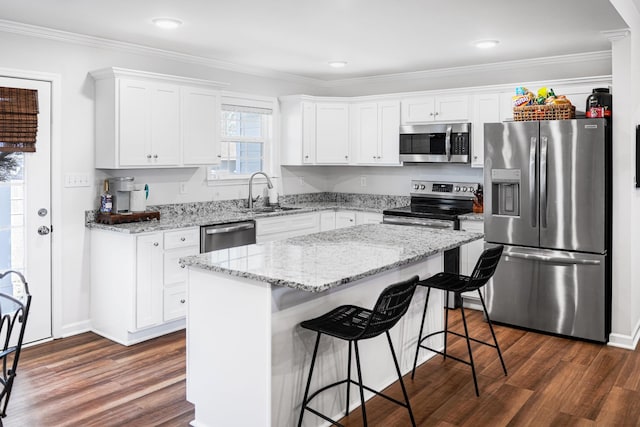 kitchen with dark wood-type flooring, crown molding, a breakfast bar area, appliances with stainless steel finishes, and white cabinets