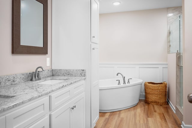 full bath with a wainscoted wall, a stall shower, wood finished floors, a soaking tub, and vanity