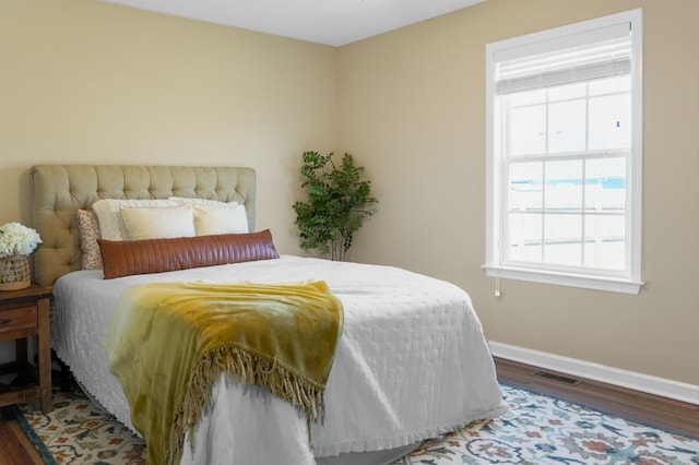 bedroom featuring visible vents, multiple windows, baseboards, and wood finished floors