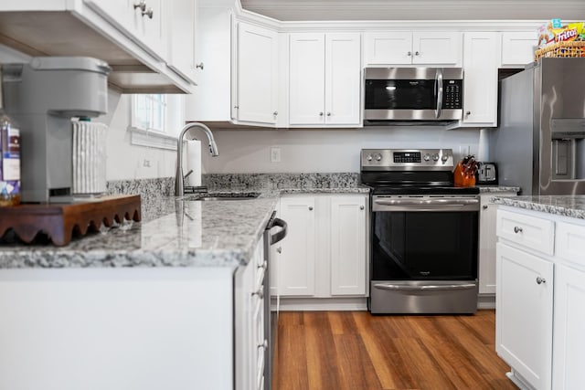 kitchen with light stone counters, wood finished floors, a sink, appliances with stainless steel finishes, and white cabinetry