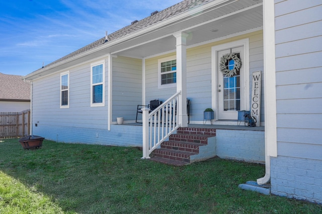 entrance to property featuring a lawn, covered porch, and fence