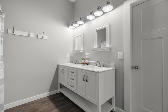 full bathroom featuring double vanity, wood finished floors, baseboards, and a sink