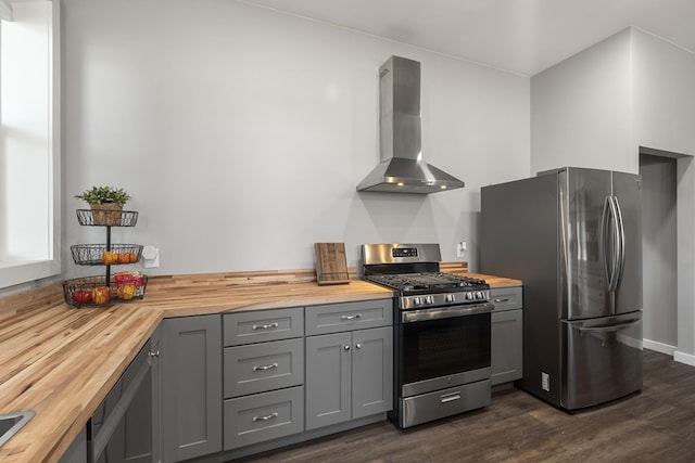 kitchen featuring gray cabinets, wood counters, dark wood-style floors, stainless steel appliances, and wall chimney range hood