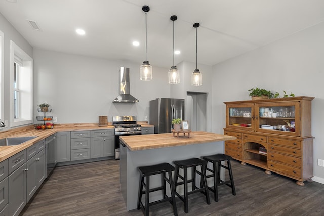 kitchen with butcher block countertops, gray cabinets, stainless steel appliances, wall chimney exhaust hood, and a sink