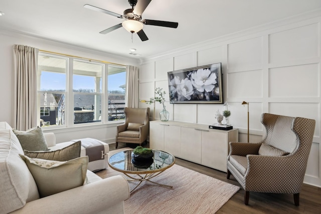 living room with crown molding, dark wood finished floors, a ceiling fan, and a decorative wall