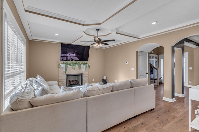 living room with ornamental molding, a ceiling fan, arched walkways, light wood-style floors, and a fireplace