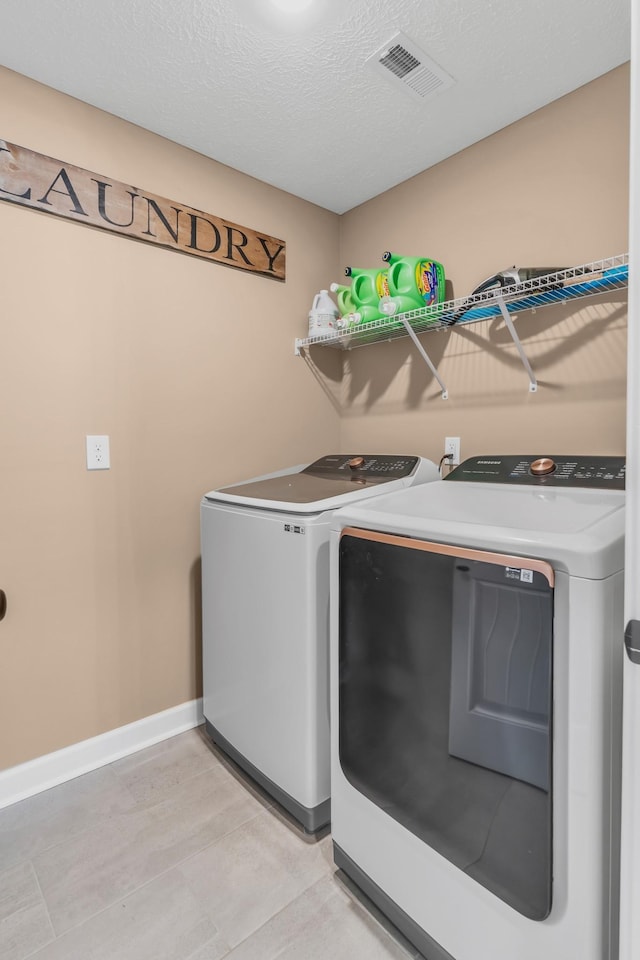 laundry area featuring visible vents, a textured ceiling, washing machine and dryer, baseboards, and laundry area