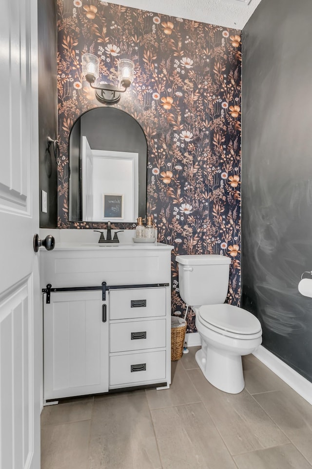 half bathroom with tile patterned flooring, toilet, wallpapered walls, and vanity