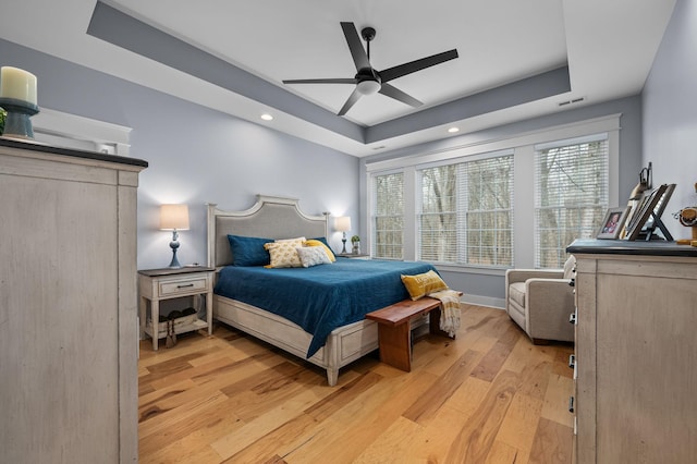 bedroom featuring visible vents, light wood-style flooring, a ceiling fan, a tray ceiling, and baseboards