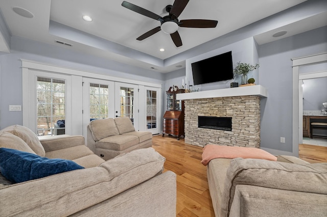 living room featuring visible vents, a raised ceiling, wood finished floors, and a ceiling fan