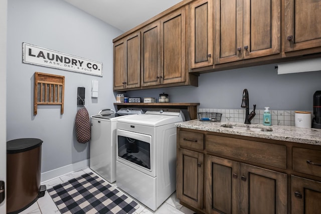 clothes washing area featuring baseboards, cabinet space, independent washer and dryer, and a sink