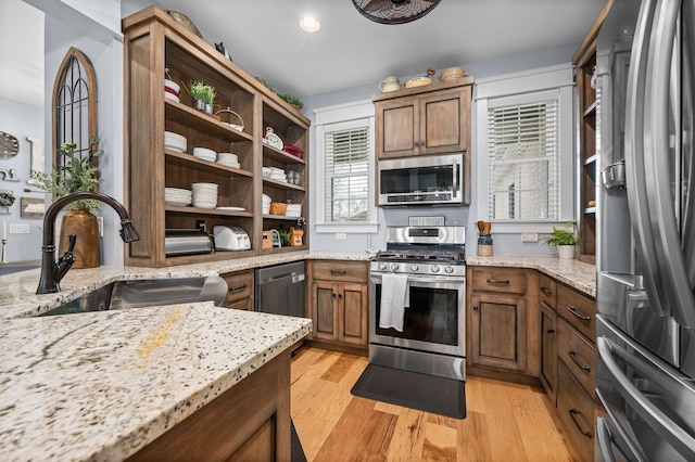 kitchen with light stone counters, open shelves, a sink, stainless steel appliances, and light wood-type flooring