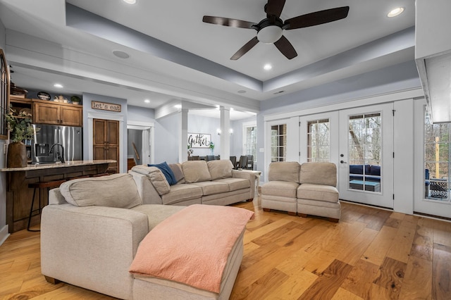 living area featuring a ceiling fan, recessed lighting, light wood-style floors, french doors, and a raised ceiling