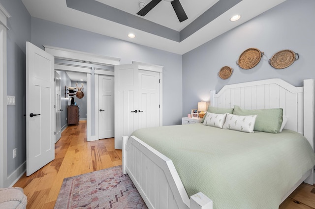bedroom with baseboards, ceiling fan, recessed lighting, light wood-style flooring, and a raised ceiling