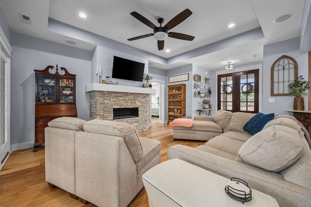 living area with light wood-type flooring, visible vents, a ceiling fan, french doors, and a stone fireplace