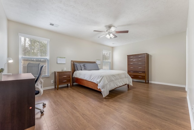 bedroom featuring visible vents, multiple windows, a textured ceiling, and wood finished floors