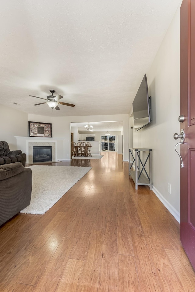 living area featuring baseboards, ceiling fan with notable chandelier, a glass covered fireplace, and light wood finished floors