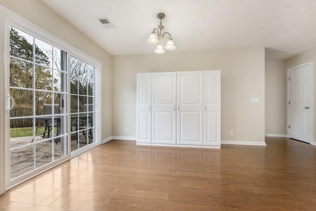 unfurnished dining area with light wood-type flooring, visible vents, baseboards, and a chandelier