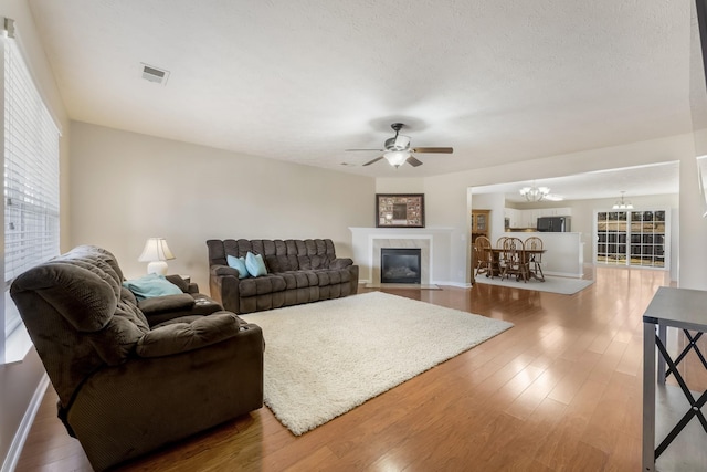 living room featuring visible vents, a fireplace with flush hearth, ceiling fan with notable chandelier, wood finished floors, and a textured ceiling