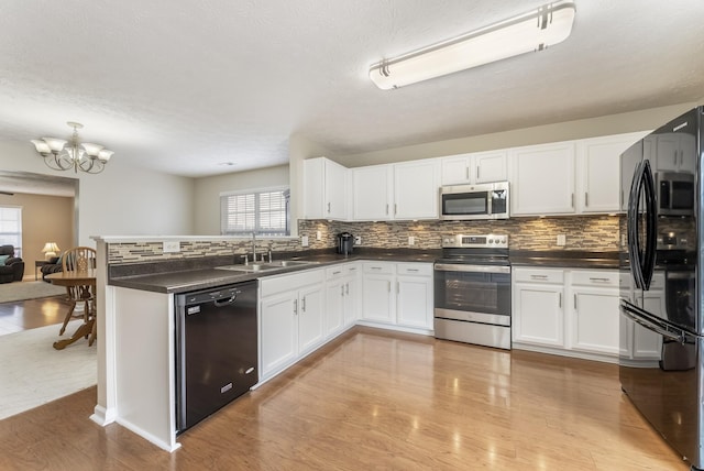 kitchen with black appliances, a sink, dark countertops, a peninsula, and white cabinets