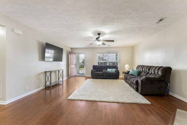 living area featuring visible vents, baseboards, wood finished floors, a textured ceiling, and a ceiling fan