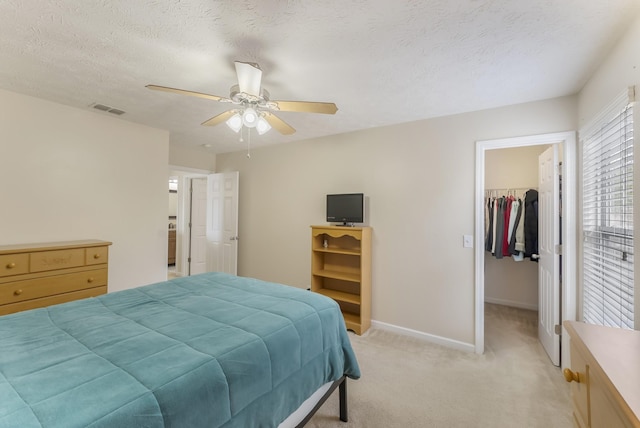 bedroom featuring visible vents, a walk in closet, a textured ceiling, baseboards, and light colored carpet