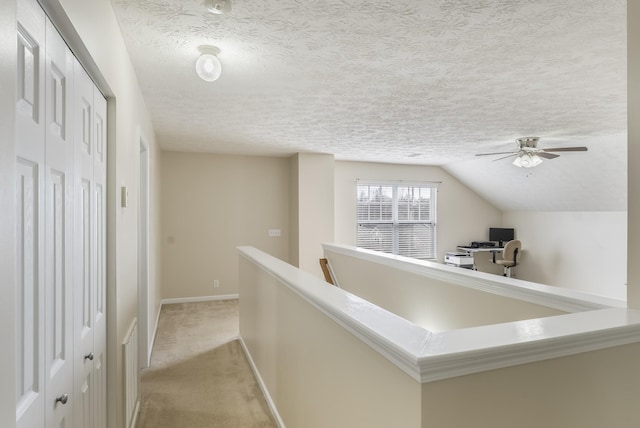 hallway with baseboards, light colored carpet, vaulted ceiling, an upstairs landing, and a textured ceiling